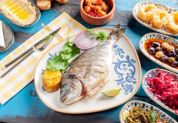 A vibrant Mediterranean meal featuring grilled fish and assorted appetizers on a rustic table.
