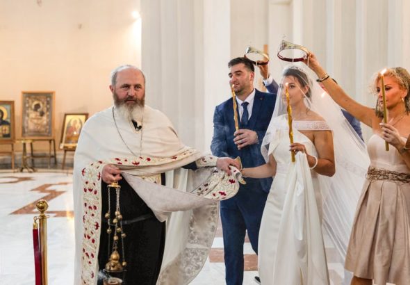 A traditional wedding ceremony with priest, bride, groom, and guests inside a church.